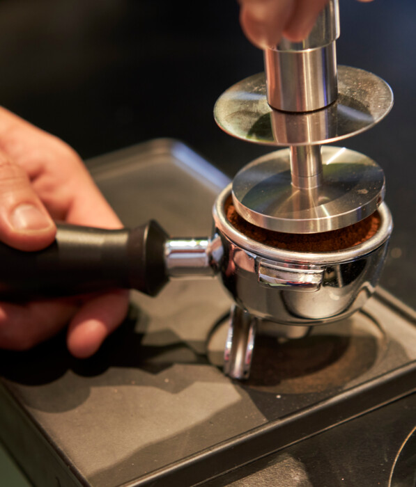 Ein Barista presst Kaffeepulver in einem Siebträger fest.