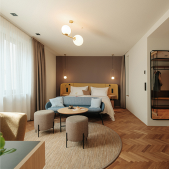 Gemütliches Circular Living Zimmer mit Doppelbett, blauem Sofa, zwei runden Hockern und rundem Teppich aus alten Fischernetzen und Recycling-Plastik und historischem Parkett mit Fischgrätmuster.