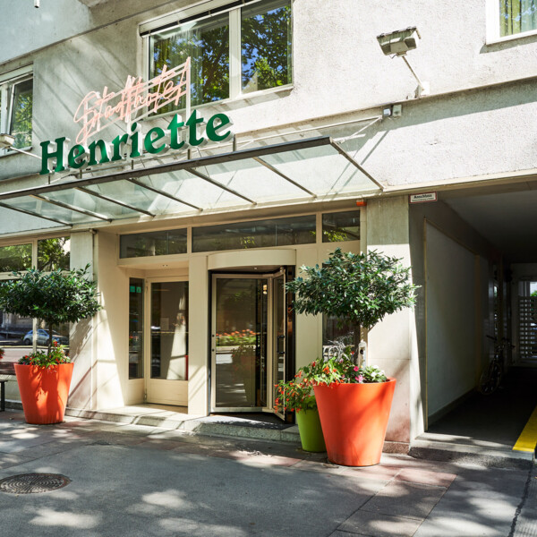 Eingang des Hotels Henriette mit Glasdach und großen Pflanzkübeln.