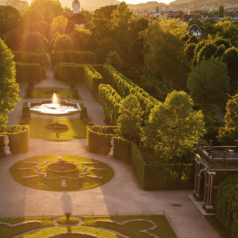 View of Schönbrunn Palace Park in Vienna with symmetrical hedges, fountains, and pathways in warm evening light.