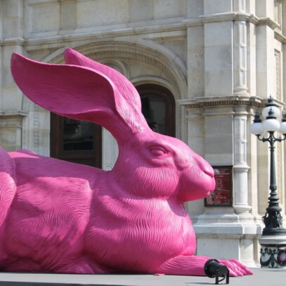 Large pink sculpture of the Dürer Hare in front of the historic Viennese opera house.