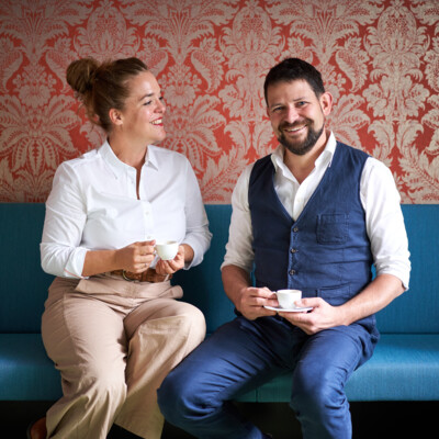 Verena und Georg Pastuszyn mit einer Tasse Kaffee im Frühstücksraum sitzend.