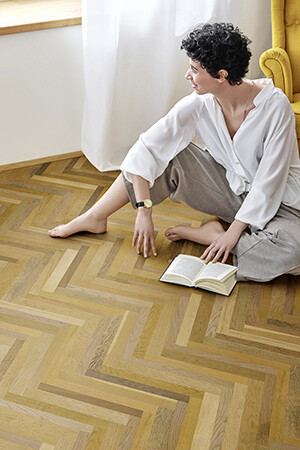 Woman sitting on the parquet floor – rescued and refurbished by Weitzer Parkett. © Weitzer Parkett