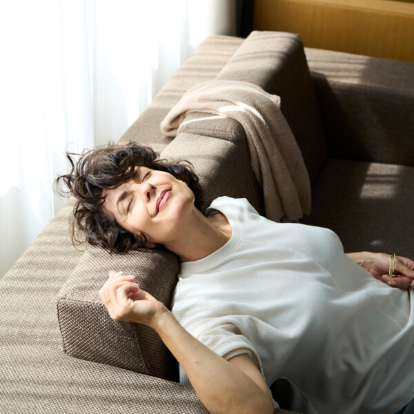 A woman sits on the sofa, enjoying the healthy atmosphere of her Circular Living hotel room at Henriette in Vienna.