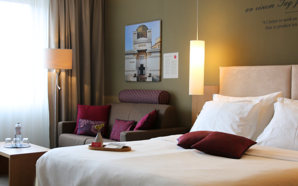 Helles Hotelzimmer mit Doppelbett, Sofa und Wandkunst im Henriette Stadthotel, Wien.