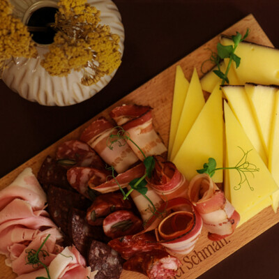 A large cold platter of meat, sausage and cheese served on a wooden board.
