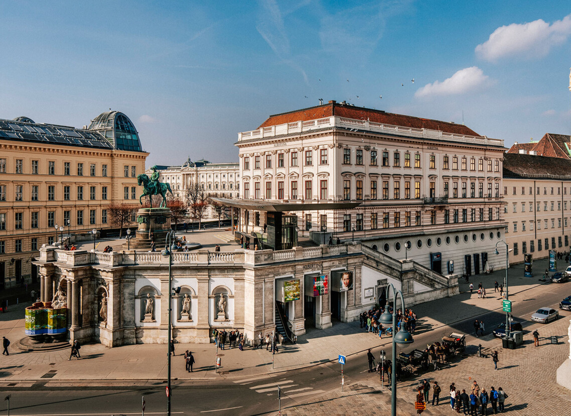 Das Albertina-Museum in Wien, umgeben von klassischer Architektur und einer belebten Straße mit Menschen und Autos.