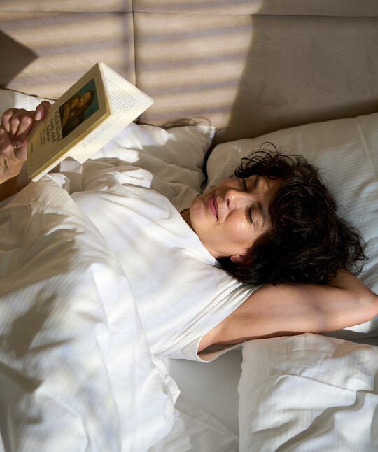 Dame beim Lesen eines Buches im gemütlichen Bett des Hotel Henriette in Wien - ehemals Hotel Das Capri.