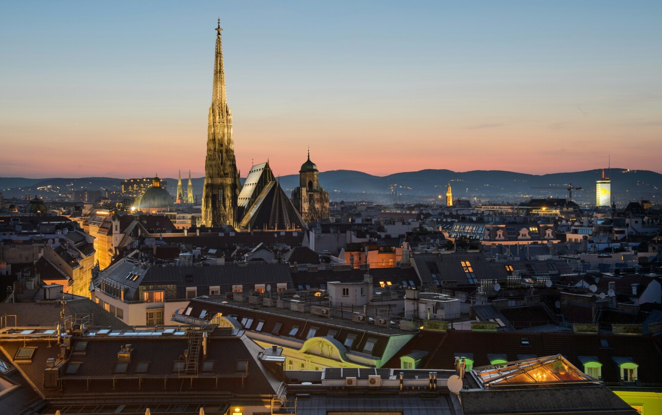 Vienna cityscape at sunset with St. Stephen's Cathedral and surrounding rooftops, viewed from above.