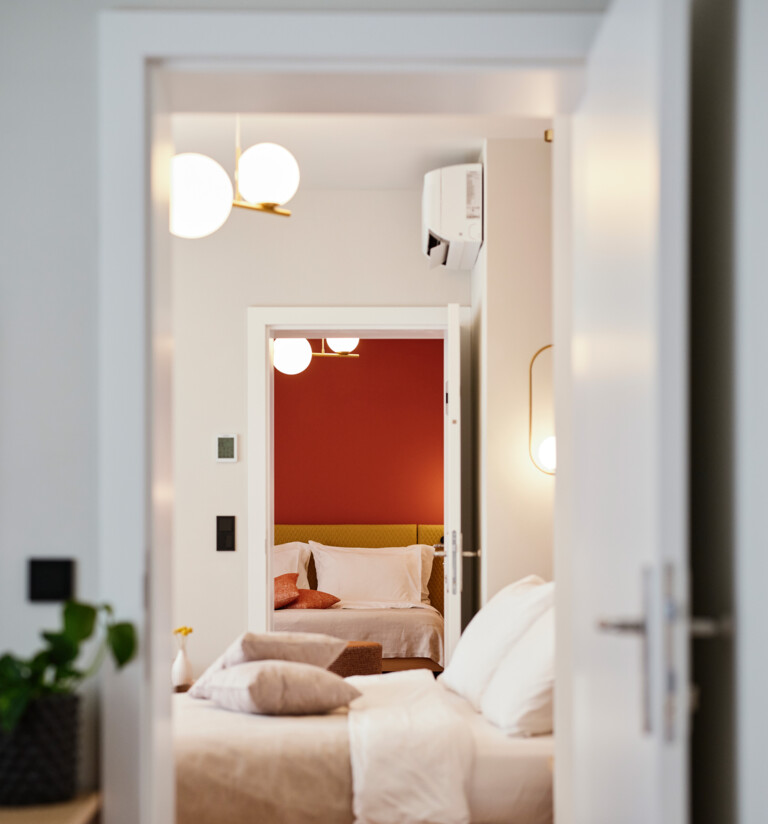 Blick durch geöffnete Türen in ein stilvolles Schlafzimmer mit weißen und roten Akzenten im Henriette Stadthotel.
