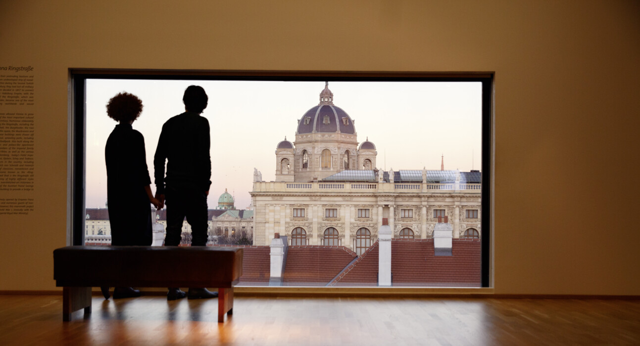 Pärchen blickt vom Panoramafenster des Leopoldmuseums im MQ auf das Kunsthistorische Museum in Wien