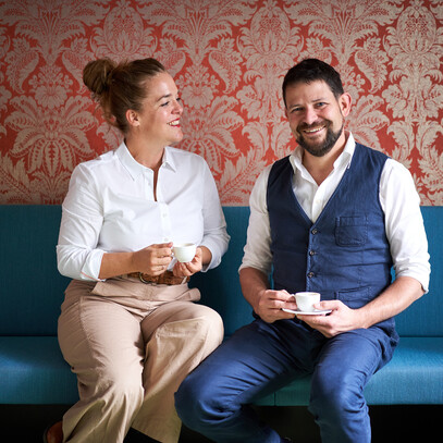 Verena and Georg Pastuszyn sitting on a couch with a cup of coffee.