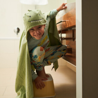 Ein Kind in Dinosaurier-Kostüm steht lächelnd auf einem Hocker im Badezimmer des Henriette Stadthotels.