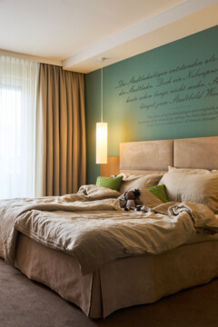 Gemütliches Hotelzimmer im Henriette Stadthotel mit Doppelbett, Sessel, Tisch und sanfter Beleuchtung. Elegantes und einladendes Ambiente.