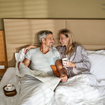 Pärchen beim Ausruhen im Bett in den großzügigen Zimmer des 4* Hotels Henriette nahe den Christkindlmärkten in Wien.