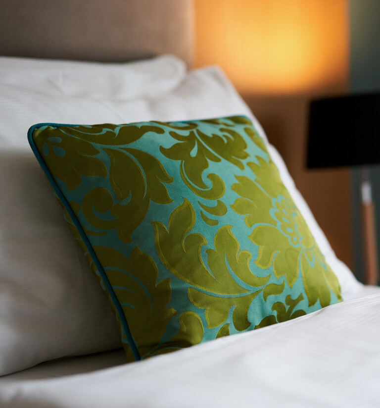 Double bed with green pillow – relax in our hotel rooms in the centre of Vienna.