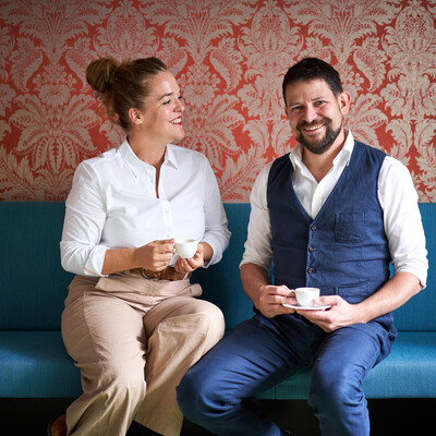 Verena und Georg Pastuszyn mit einer Tasse Kaffee auf einer Couch sitzend.