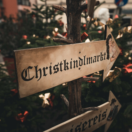 Sign pointing to Christkindlmarkt with decorated Christmas trees in the background.