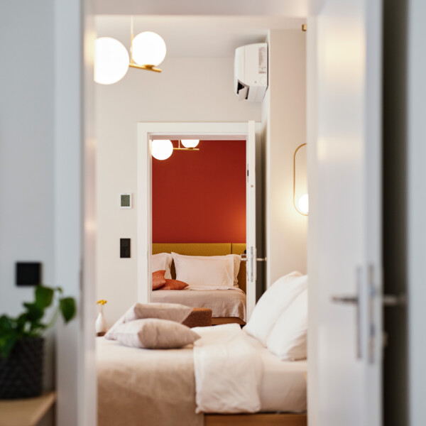 Blick durch geöffnete Türen in ein stilvolles Schlafzimmer mit weißen und roten Akzenten im Henriette Stadthotel.