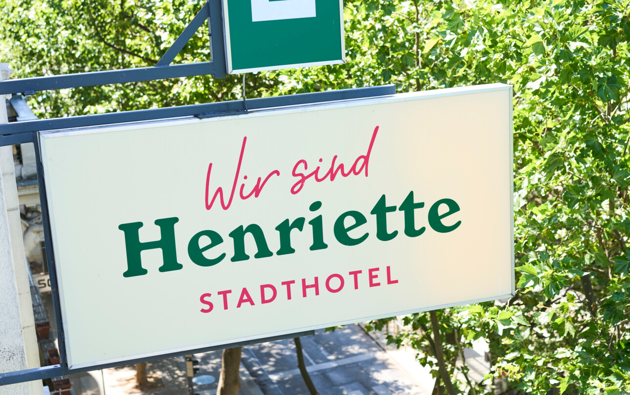 Sign for Hotel Henriette StadtHotel with green trees in the background.
