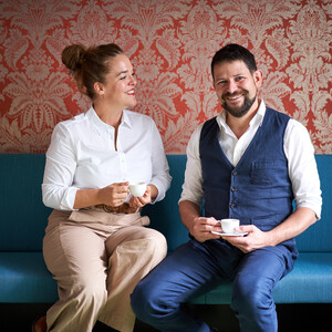 Verena und Georg Pastuszyn mit einer Tasse Kaffee auf einer Couch sitzend.