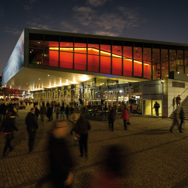 Die Wiener Stadthalle leuchtet nachts in Rot, während Besucher ankommen; ein Tipp für Gäste des 4* Stadthotel Henriette.