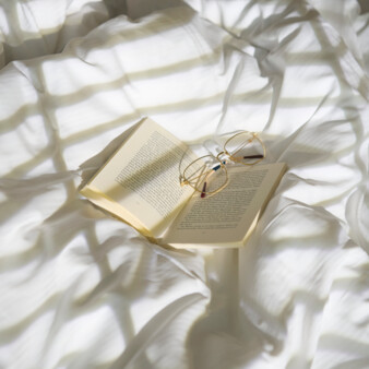 An open book with gold-rimmed glasses rests on a crumpled white organic cotton bedspread at Stadthotel Henriette.